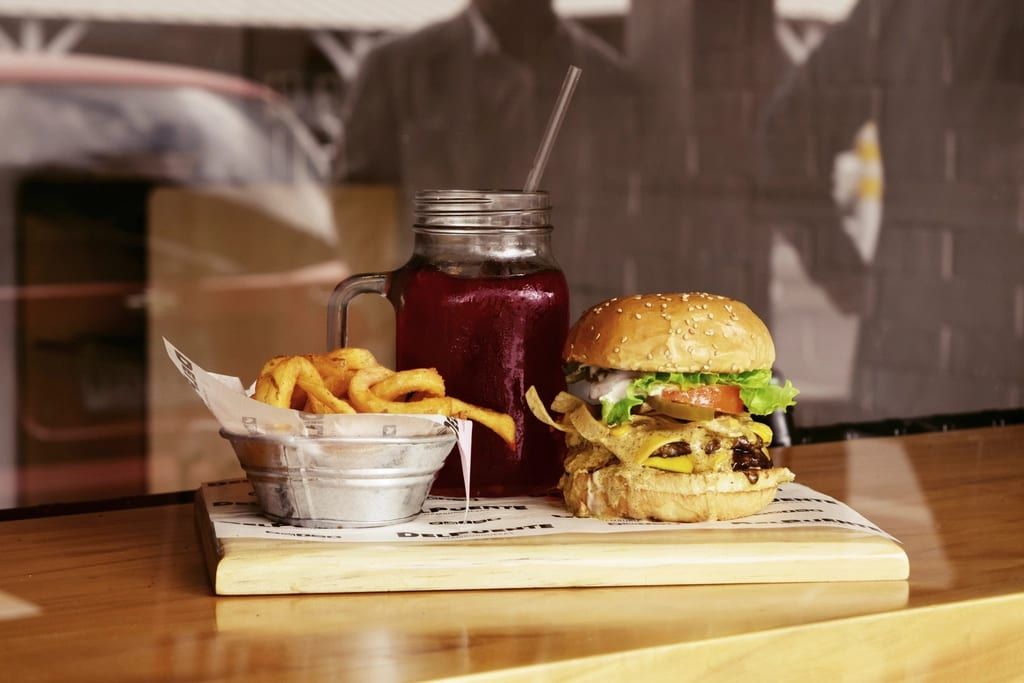 A burger with a basket of fries and a jar of red juice on a wooden board