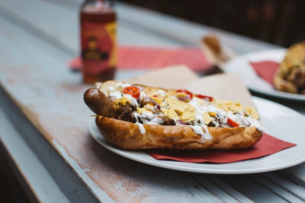 A hot dog loaded with sauce, crushed chips and peppers on a plate