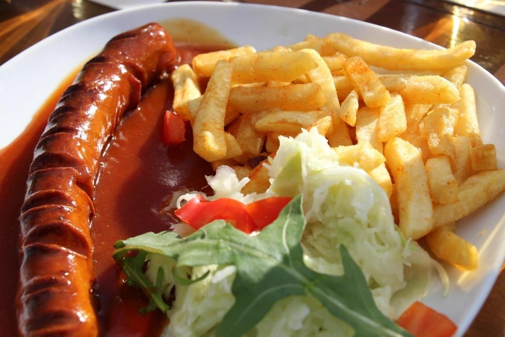 A grilled sausage with fries and salad on a plate