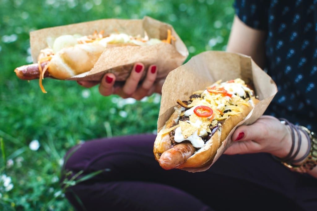 Two people holding loaded hot dogs wrapped in paper outdoors